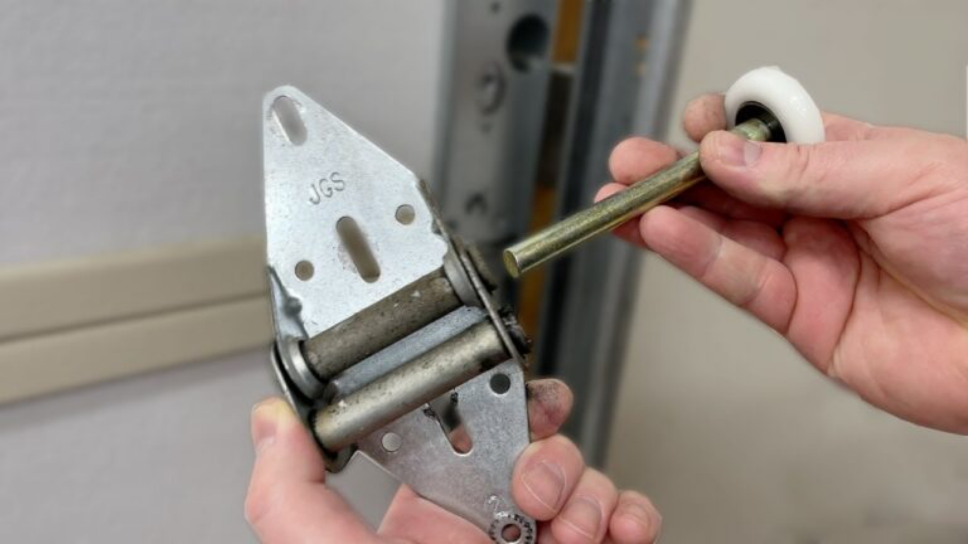 A man holding a garage door hinge and roller